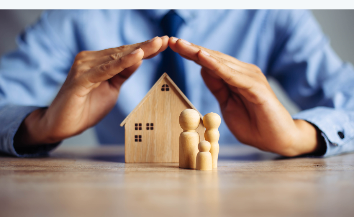 Manos protegiendo una casa y figuras de una familia, simbolizando un seguro